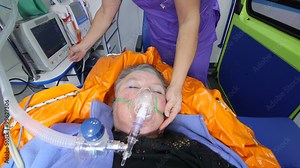 Emergency medical service paramedic monitoring critical senior patient condition in ambulance using heart monitor, directly above jib crane shot camera moving up/down