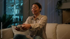 African American woman female gamer playing online video game on couch night insomnia ethnic girl having fun play videogame using joystick controller gaming console on TV at home cyber entertainment