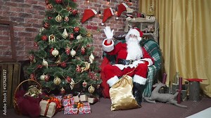 Santa waving his hand while sitting in a chair at the Christmas tree
