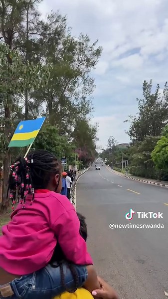 A young fan seen across the street waving the Rwandan flag cheering on riders.