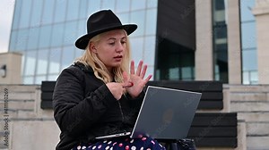 Young woman speaks sign language on a video call on a laptop outdoors. The deaf-mute girl communicates with gestures
