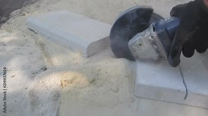 The process of cutting a concrete slab into pieces by an angular grinder - 15s. A man in protective gloves cuts a concrete product with an electric circular saw outdoors in the dust