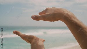 Close-up man moving hands as if controlling power of sea waves. Strange dance hand of male person on sea coast. Chi Kung energy control. Exercises hands on background of wave on a sunny day