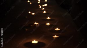 Many burning candles in the dark. A path of lit small candles in a black room. The concept of new life, rebirth, remembrance of the dead. High quality 4k footage