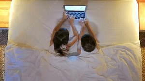 Children play on the computer in the bed under the blanket at night. Computer games. View from above.