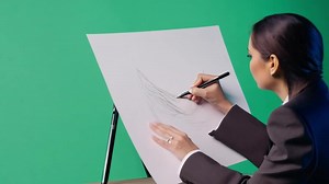 Download A fashion designer in a stylish outfit, sketching designs. Green screen backdrop. Soft, diffused lighting to reflect a design studio. for free