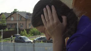 Upset woman holds her head in her hands and looks down standing on the balcony. Headache, migraine, blood pressure, stress. Close-up