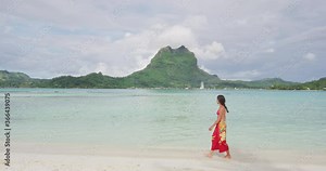 French Polynesia Vacation Travel woman walkijg on paradise motu beach on holidays on Bora Bora with Mount Otemanu. Happy girl wearing traditional pareo and Bikini in Tahiti, French Polynesia.