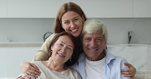 Optimistic beautiful multi generational family portrait concept. Loving millennial daughter hugs elderly mother and father smile pose look at camera, feel happy enjoy time together and warm relations