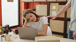 Tired man and woman workers, keystroking away on a laptop together, struggle to stay on point in a drab office setting