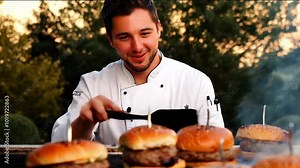 Handsome chef smiling behind grill while cooking sizzling burgers on outdoor grill. The chef and the burger will be in the middle of the video. The burger will be along the chef's chest.