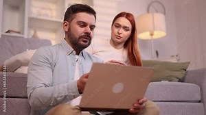 Smiling young couple looking at laptop computer screen choose products in online internet store make order online booking or plan trip at cozy home Happy people enjoying time together indoors