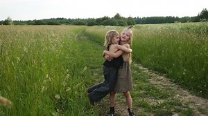 two girls sisters in dresses hugging in a field at sunset in summer