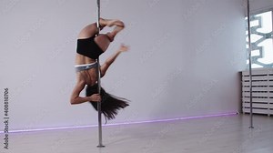 Pole dancing in the studio - brunette woman spinning on the pole upside down
