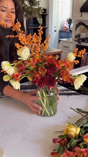 Simple, affordable, and so festive. ♥️🌼✨ DIY Thanksgiving Bouquets with Trader Joe’s Flowers 🦃 My biggest tip? Make a tape grid on your vase. It keeps every stem in place and instantly makes your arrangement look professional — even with little hands tugging at your sweater while you do it. 😉 DIY Thanksgiving Bouquets with Trader Joe’s Flowers: • Red chrysanthemum bunch — $4.99 • Yellow autumn peony tulips — $8.99 • Orange alstroemeria (2 @ $4.99) — $9.98 • Orange holly ilex berries — $7.99 •
