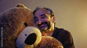 Bearded man shares tender moment with teddy bear. His genuine smile and playful expression create intimate atmosphere. Lovely giant plush toy.