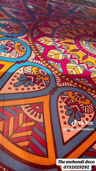 Say no to boring Mehendi decors and make way for creative setups by us! This vibrant decor features a stunning Mughal-inspired backdrop in pink and orange, adorned with cascading marigold and natural jasmine garlands. A plush beige loveseat with bright cushions sits amid colorful embroidered umbrellas, antique lanterns, and fresh florals. The dance floor boasts a striking rangoli-style design, while draped fabric in red and orange, along with hanging marigolds, jasmine, and embellished umbrellas