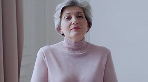 Beautiful old woman with gray hair smiles standing at home