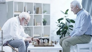 side view of two senior men playing chess and pressing button on chess clock in living room
