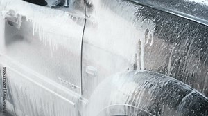 Slow Motion Video of a Car Washing Process on a Self-Service Car Wash. A Jet of Water With a High Pressure Wash Off the Dirt From the Car. Side View. Foamed Detergent Drains From the Surface of the