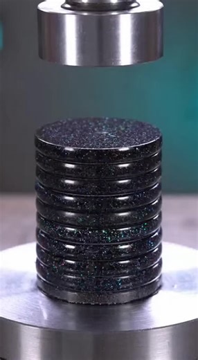 A tall stack of dark composite gaming tokens with obsidian and metallic flecks gets slowly crushed under a hydraulic press. Watch as the tokens bow, slide out of alignment, and pancake smoothly while translucent dark binder oozes out in this ultra-satisfying ASMR destruction. | Nic Davis