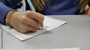 Close-up of a teenage girl's hand writing pencil and pen on paper. A child writes with a pen in a notebook during an English lesson at school.