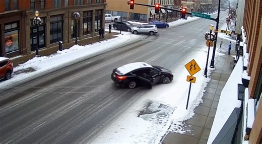Car Loses Control on Icy Intersection, Slides Into Snowbank February 2, 2026 — A routine winter commute turned hazardous when a sedan lost traction on an icy downtown intersection and slid sideways across multiple lanes before coming to rest near the curb. Traffic camera footage shows the dark-colored car entering the intersection at moderate speed as snow and ice cover the roadway. As the driver attempts to turn, the vehicle suddenly fishtails, rotating nearly perpendicular to traffic. The car 