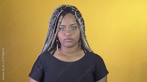 Beautiful young African American woman with dark curly dread hair, has serious and mysterious expression on face, poses in studio yellow background.