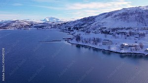 Snow covered mountain range on coastline in winter, Norway. Surroundings of town Tromso. Panoramic aerial view landscape of nordic snow cowered mountains, houses and ocean. Troms county, Fjordgard