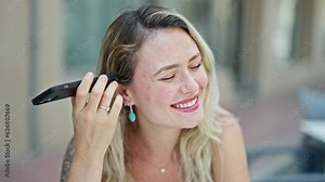 Young blonde woman listening to voice message sitting on table at coffee shop terrace