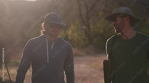 Male fly fishing hiker friends walk and laugh on trail during golden hour with fishing rods