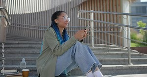 young african american woman student typing writing message on the mobile phone while sitting outdoors on steps