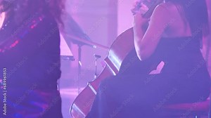 Woman cellist playing a parry on stage with bright lights and smoke show. Close-up of the instrument and the girl's hands. Professional musician playing as part of an orchestra