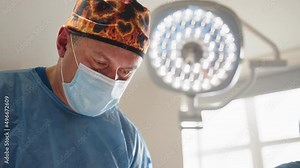 Low angle view of Caucasian male surgeon performing operation in operation theater. Caucasian surgeon male healthcare professional in a hospital operating theatre wearing a surgical cap and mask