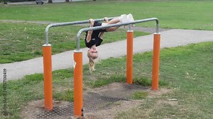 A young child shows off amazing skills by flipping upside down on monkey bars in an open park on a sunny day.