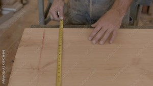 Lumber is measured with a tape measure in a wood shop by a craftsman