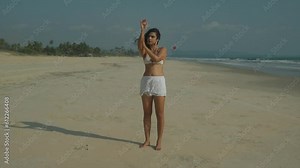 Handheld full length clip of woman applying suntan lotion to arms and hands, on sandy beach in summertime Stock Video