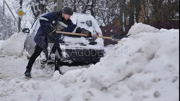 Man clearing snow around a car during heavy snowfall in winter