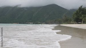 waves gracefully roll onto the sandy beach of Con Dao Island, Vietnam. Mountains can be seen in the background. low-angle perspective,