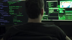 Premium stock video - Male computer hacker sitting in front of computer monitors typing code