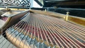 Camera moving under the opened lid of a classic older grand piano showing piano strings and stopping in front of piano keys.