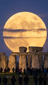 The ancients knew exactly where to stand—and on nights like this, so do we. As a golden supermoon lifts behind Stonehenge, the stones and the sky seem to lock into place, as if the entire monument was built for this one rising. The Moon swells above the trilithons, its disk so large it feels close enough to touch, while a ring of modern observers stands where people have gathered for thousands of years, watching light and shadow repeat the same cosmic pattern. Stonehenge was raised more than 5,0