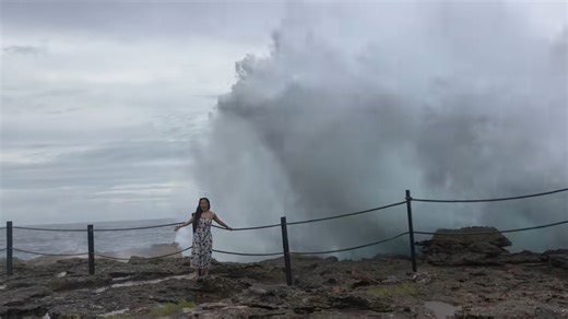 Woman gets splashed by wave on rocky shore in Lembongan Island, Bali, Indonesia