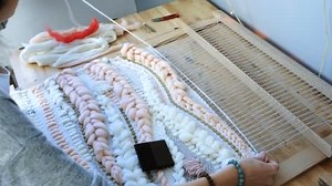 A tecer num tear. Mãos de mulher fechadas que correm em um tear. Enfiando o ônibus através dos fios de quadro e prenda o fio com vieira.