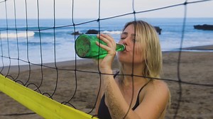 Young woman drinking on the beach. Free Stock Video Footage