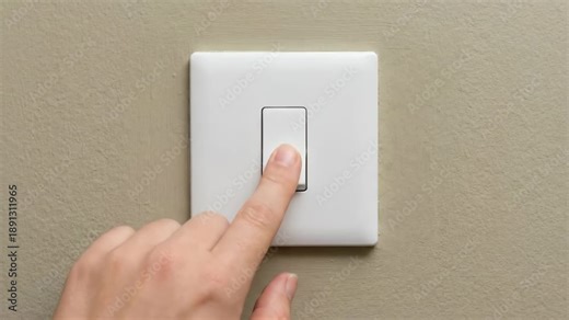 Hand pressing light switch on wall, activating light, showing gradual transition from off to on state in a modern indoor setting with neutral colors