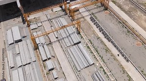 Top view of concrete pillar stacks laying on the ground in front of large warehouse construction site. Construction materials. Infrastructure themes.