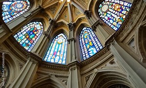 A majestic view of the interior of a historic cathedral with intricate stained glass windows through which soft natural light filters, illuminating the ornate architectural details.