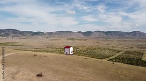 A lonely using solar panels self-contained house stands in the middle of the steppe with a view of beautiful vineyards and mountains on the horizon.