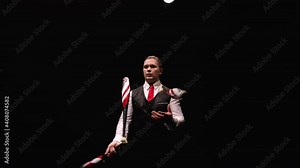 Orbital shot of a stylish man juggling with pins. The juggler hones his skill and dexterity against a black studio backdrop illuminated by lights. Professional circus show. Close up. Slow motion.